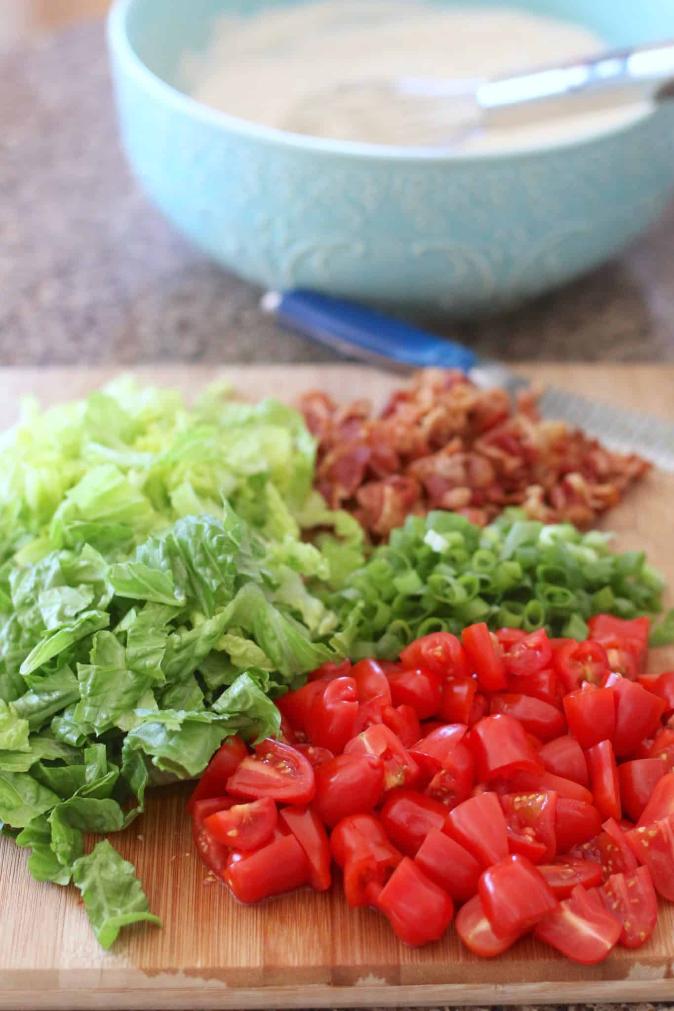 sliced cherry tomatoes, chopped romaine lettuce, chopped, cooked bacon on a wooden cutting board.