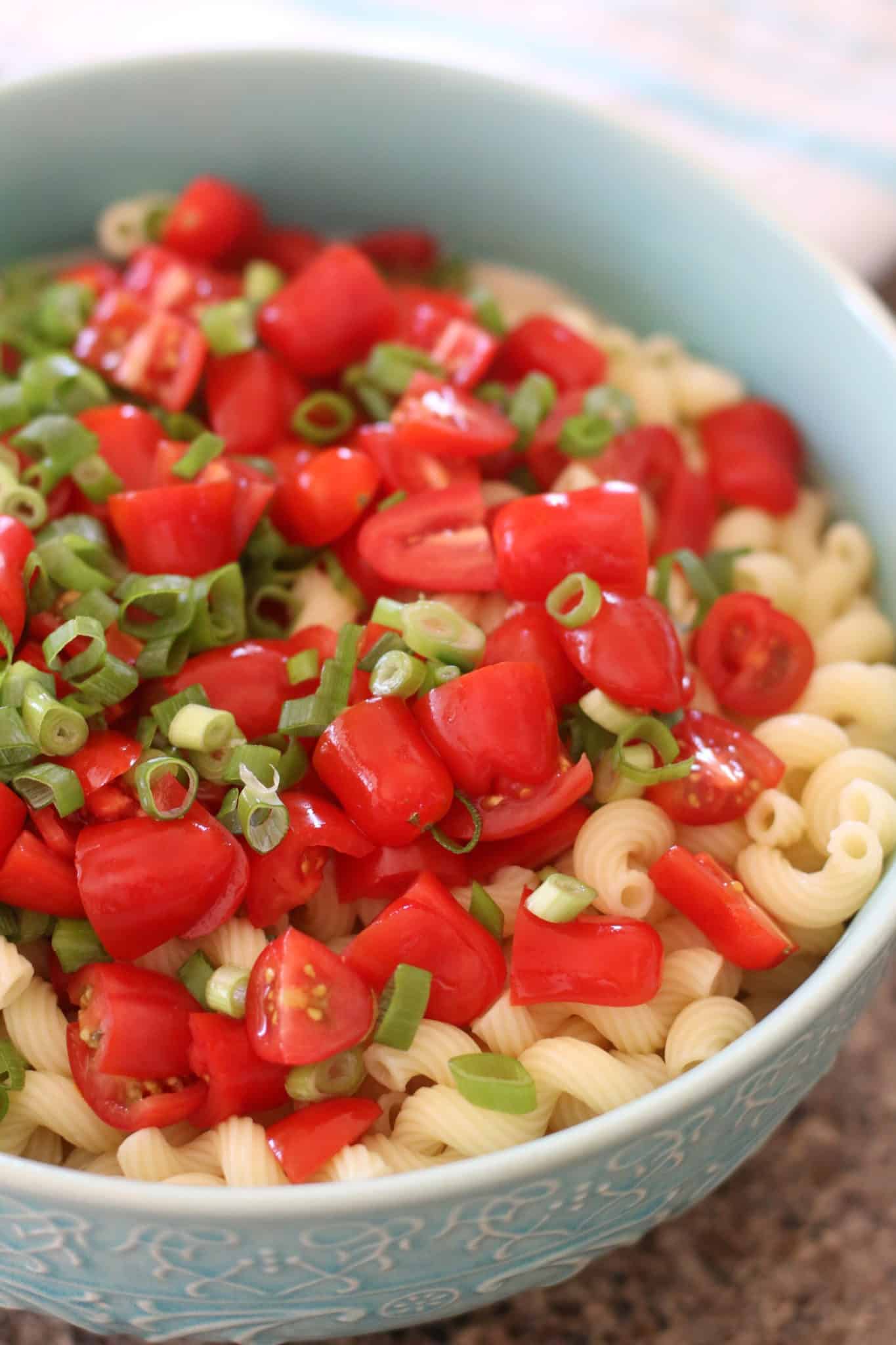cooked corkscrew pasta salad, sliced green onion, sliced cherry tomatoes in a blue bowl. 