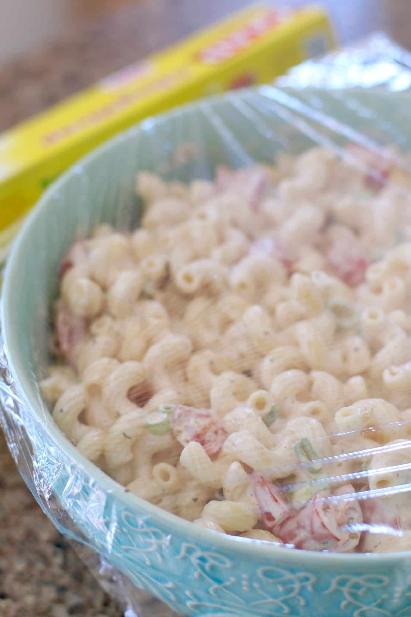BLT Macaroni Salad with dressing in a bowl covered with plastic wrap.
