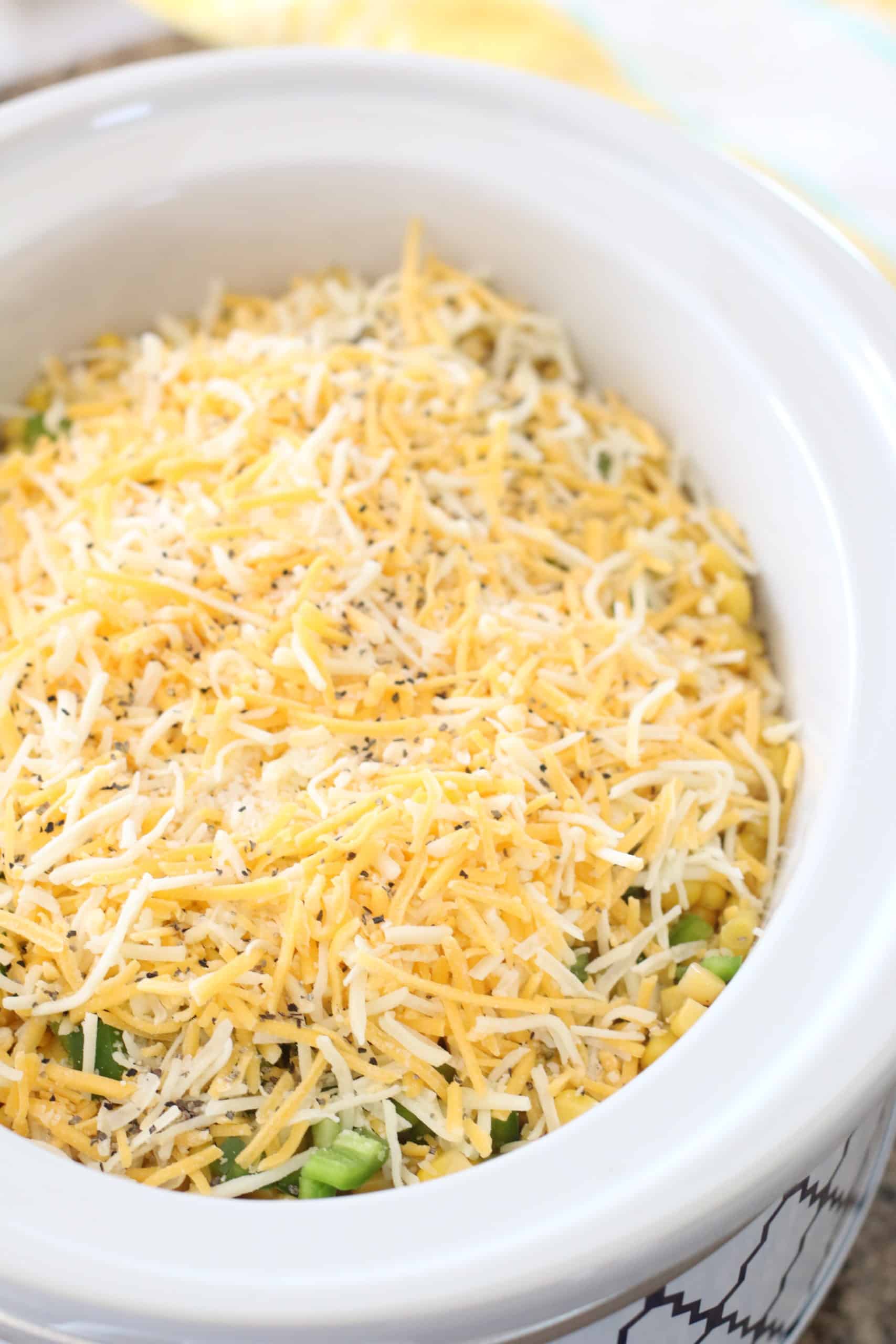 shredded Mexican blend Cheese layered on top of diced jalapeño layer in a white oval slow cooker.