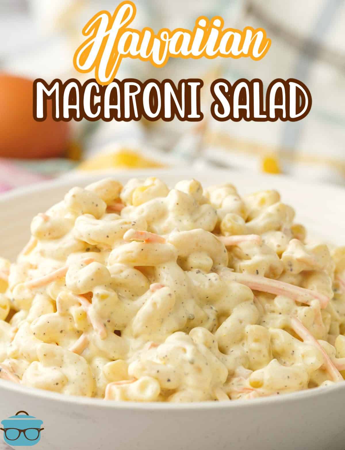 Hawaiian Macaroni Salad shown in a white bowl with a dish towel in the background.
