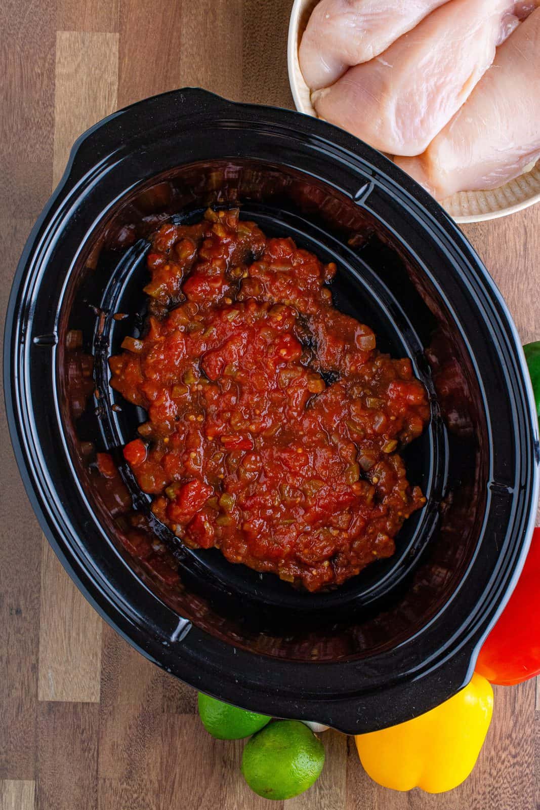 a layer of salsa shown in the bottom of a black oval slow cooker.