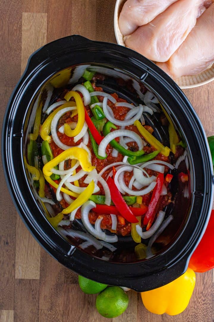sliced onions and peppers in a single layer in a slow cooker.