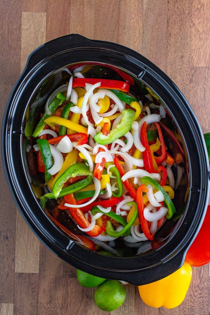 slices of onion, bell peppers sprinkled evenly on top of chicken breasts in slow cooker.