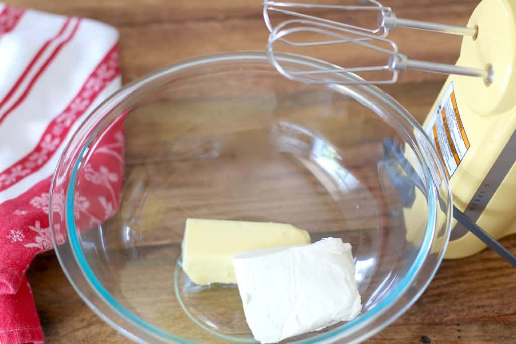 softened butter and cream cheese mixed by an electric hand mixer in a clear glass bowl.