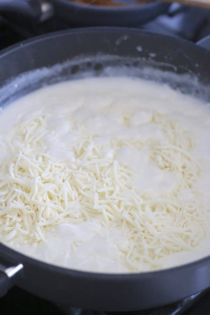 shredded mozzarella cheese added to cream sauce in large sauce pan