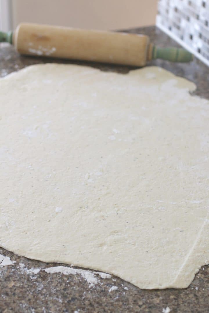 Flat, rolled out pizza dough on a countertop with a wooden rolling pin.