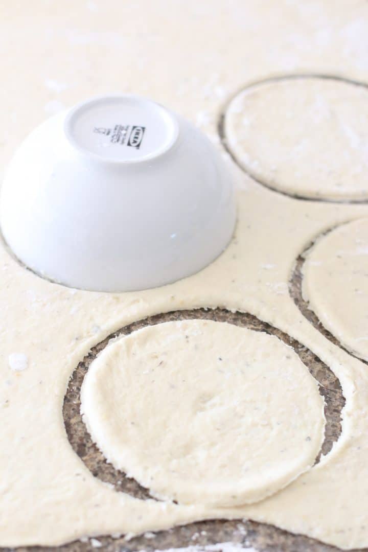 a small white bowl being used to cut out circles from pizza dough.