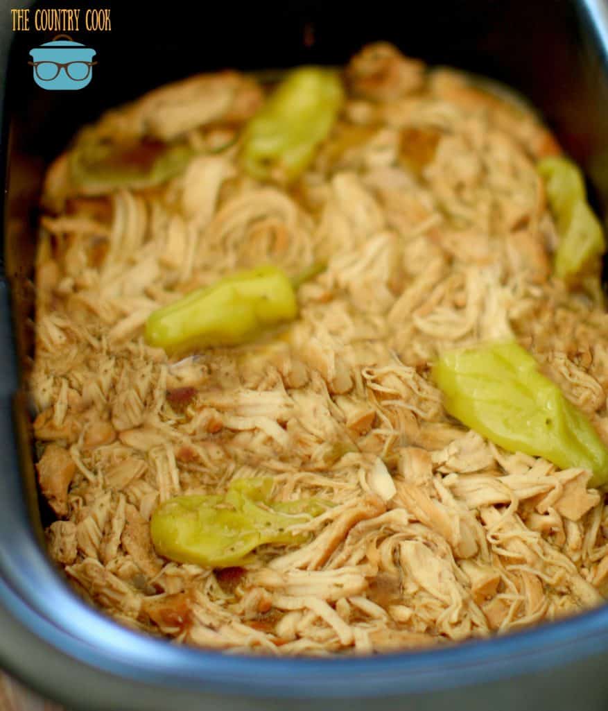 Crock Pot Mississippi Chicken, finished and shredded in a crock pot with peperoncini peppers.