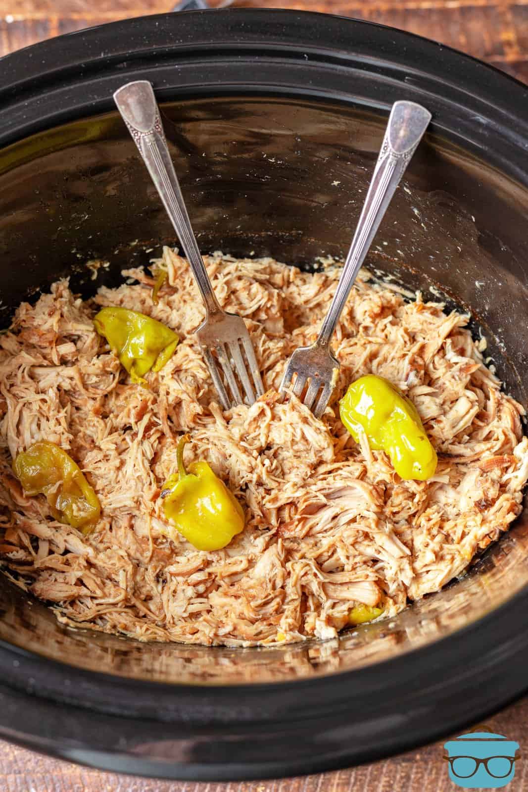 two forks in shredded chicken in a slow cooker.