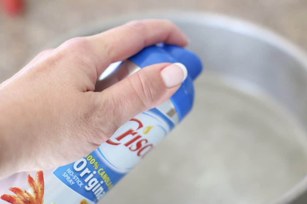 a hand spraying nonstick cooking spray into a round baking dish