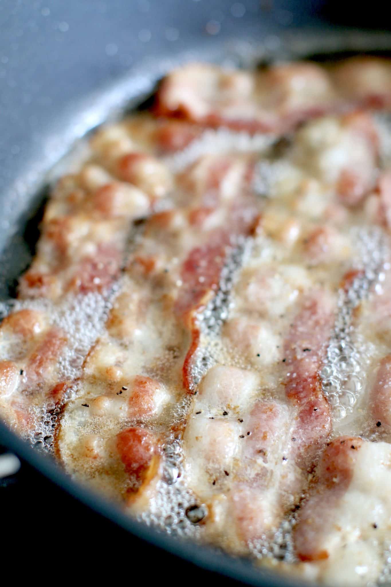 slices of bacon cooking in a pan.