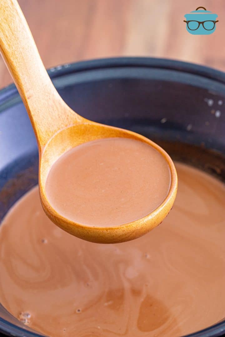 a wooden ladle scooping up hot chocolate out of a round crock pot. 