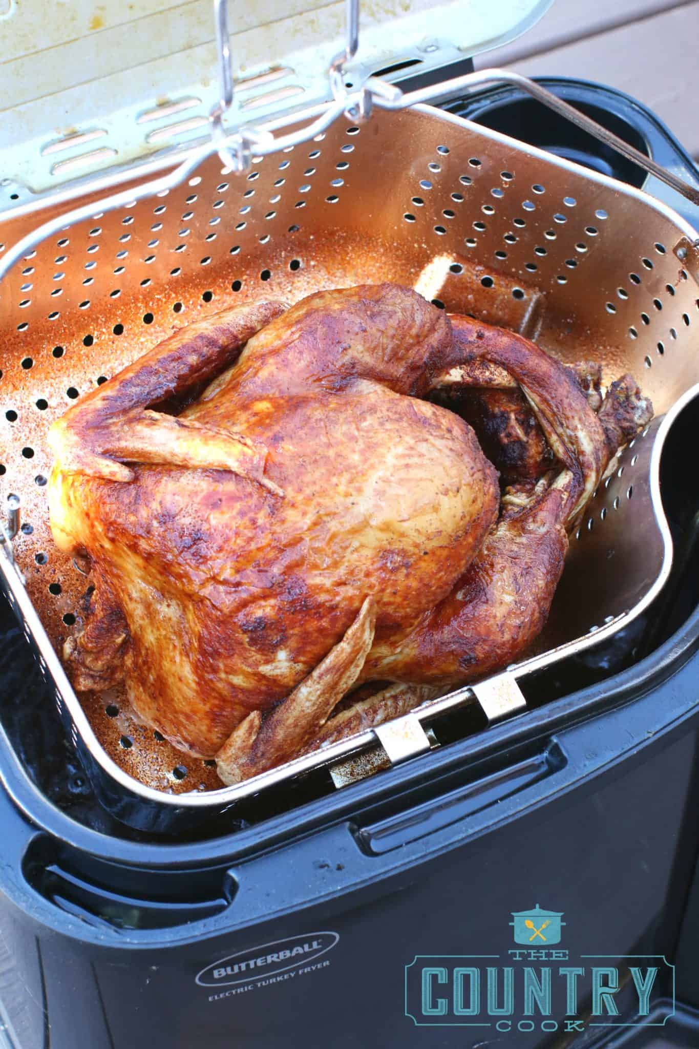 fully fried turkey being pulled up out of the frying oil of an electric turkey fryer. 
