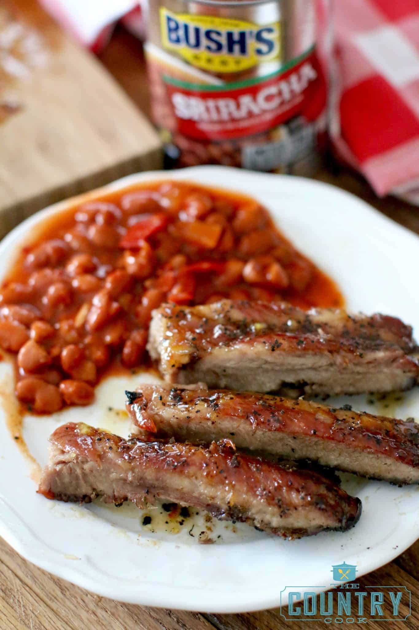 sliced pork ribs and baked beans on a round white plate.