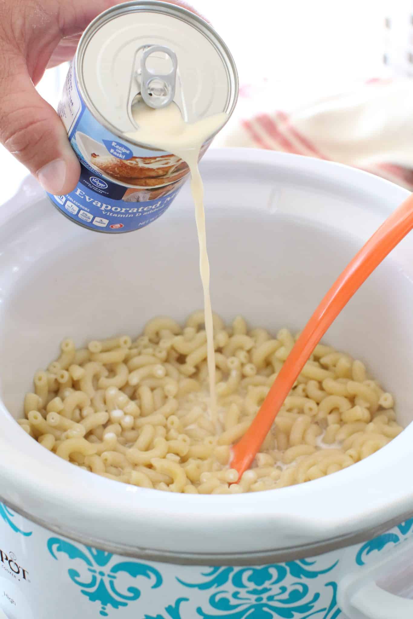 evaporated milk, half and half being poured onto the macaroni noodles in the slow cooker.