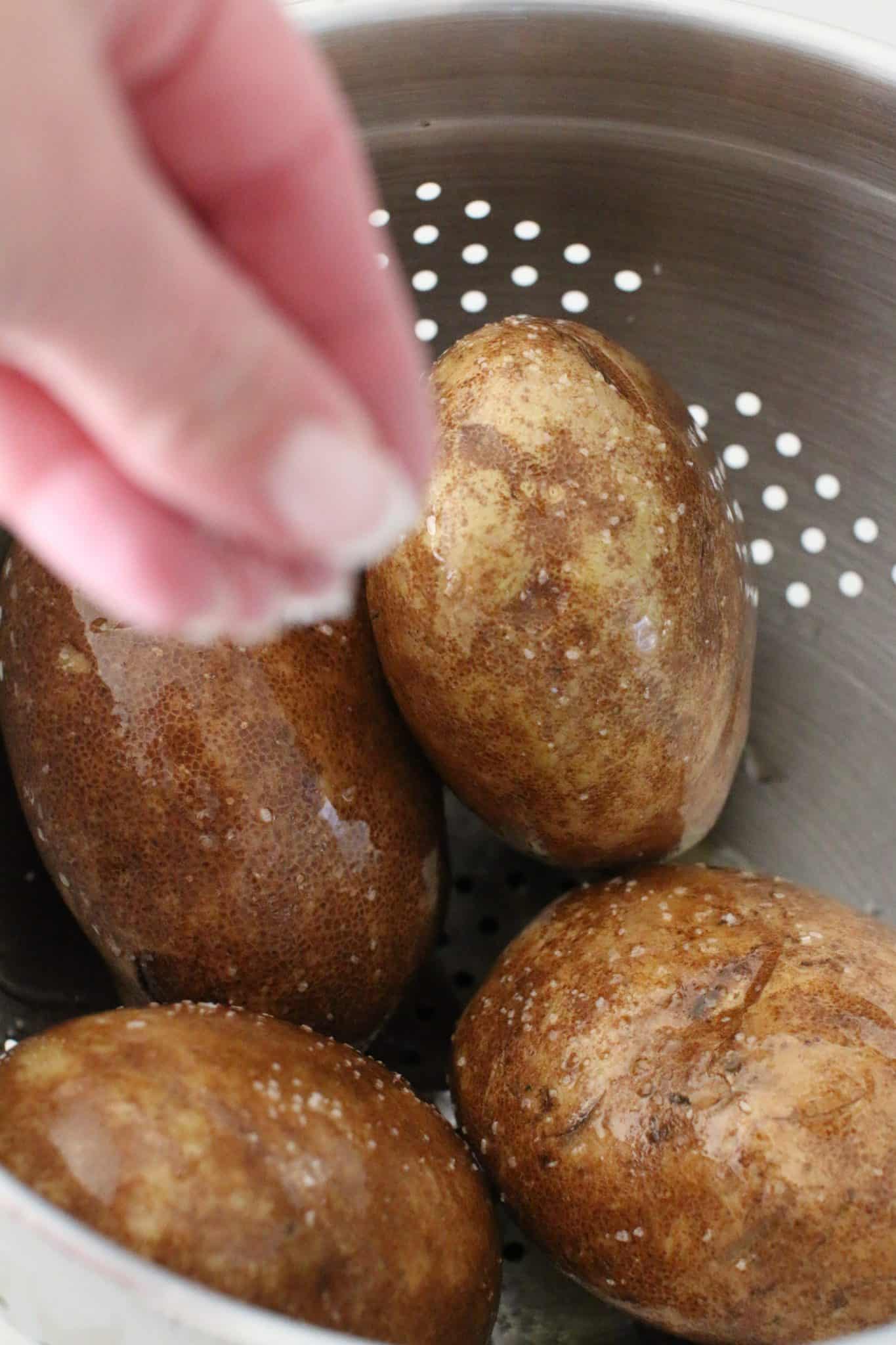 seasoning potatoes with kosher salt in a colander.