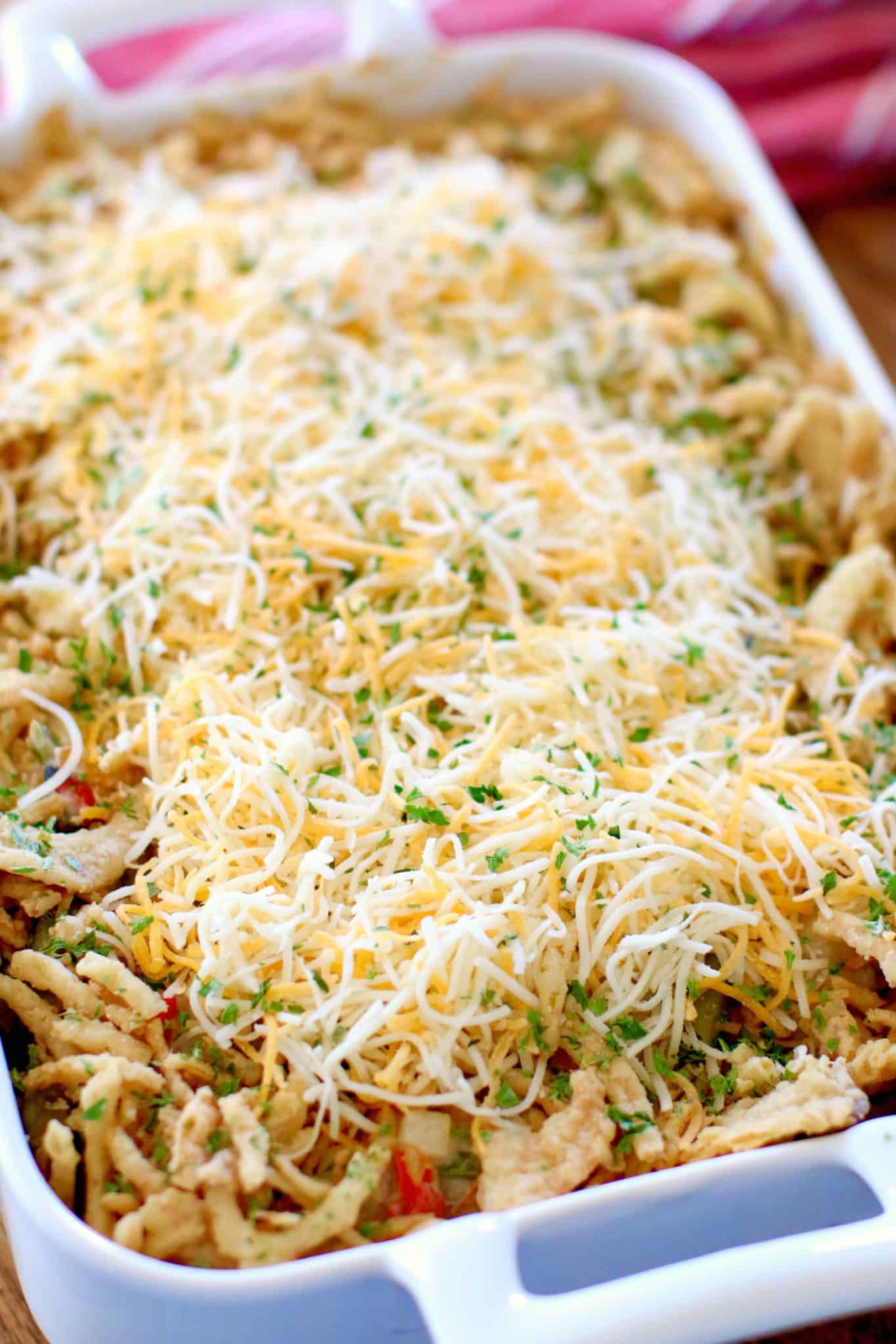 shredded cheese and crispy fried onions on top of green bean casserole mixture in baking dish.