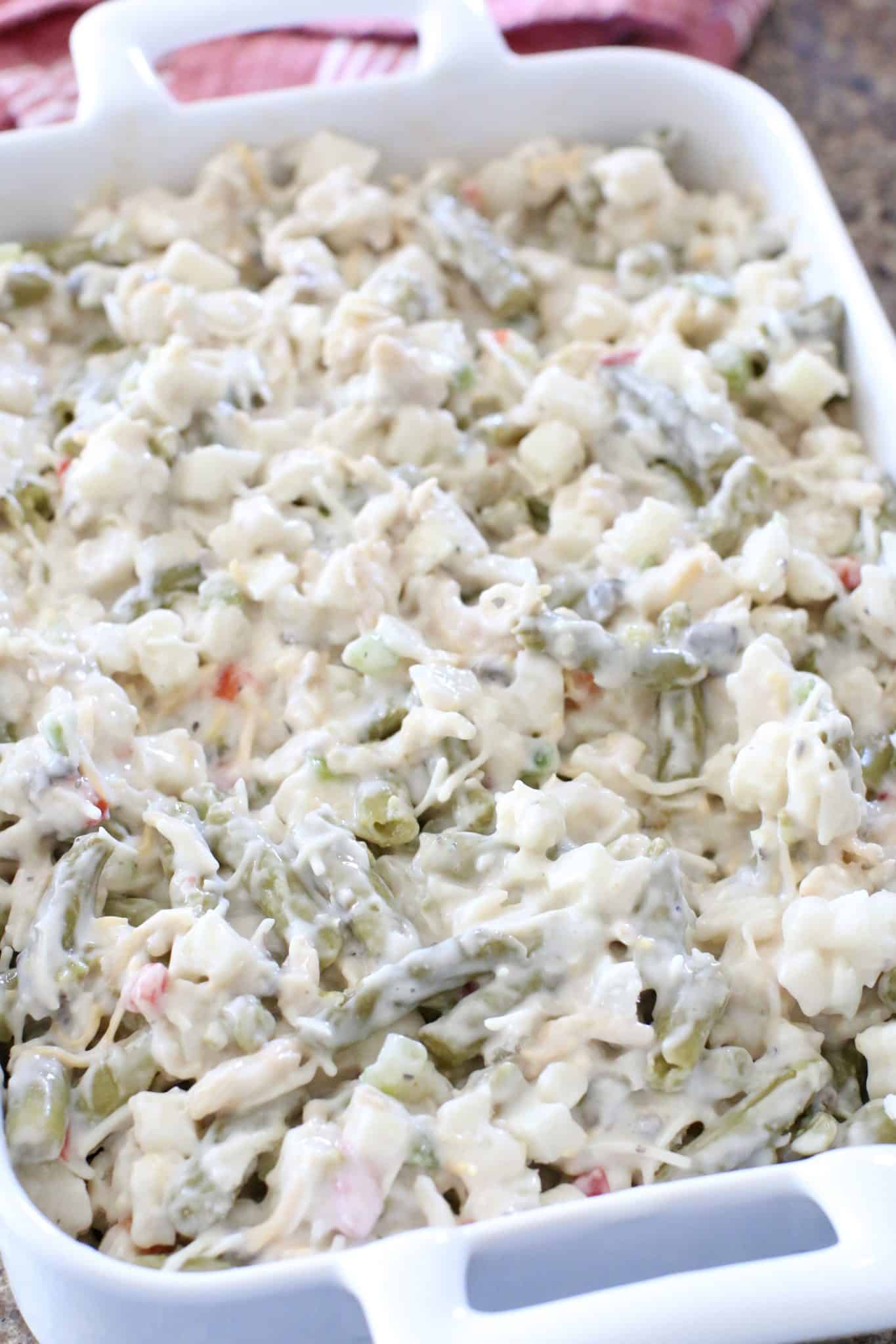 uncooked green bean casserole mixture spread out evenly in a rectangular white baking dish.