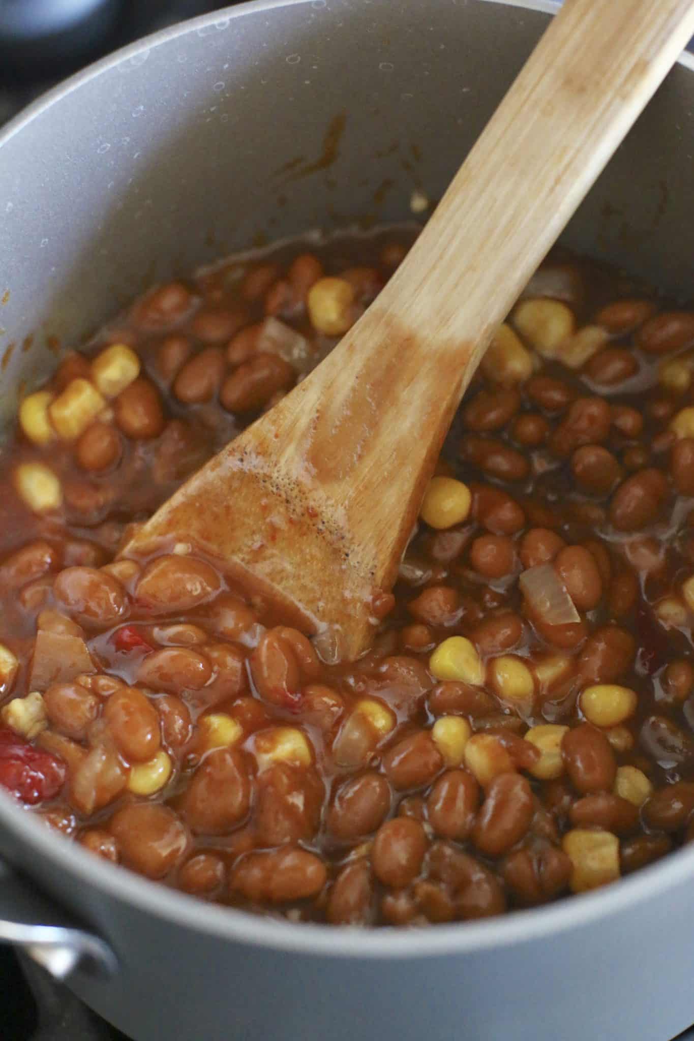 beans, corn and onions in a skillet being stirred with a wooden spoon.