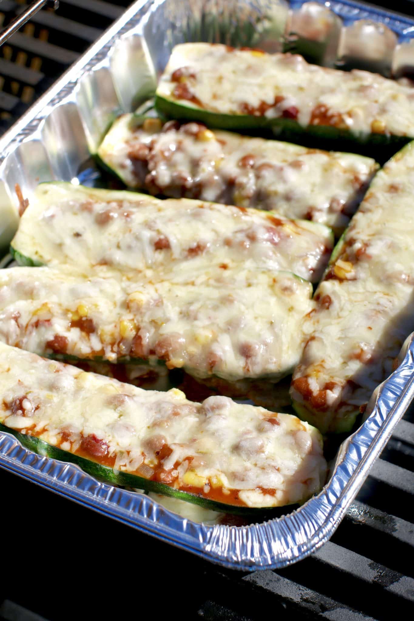 fully cooked stuffed zucchini in baking pan on the grill.