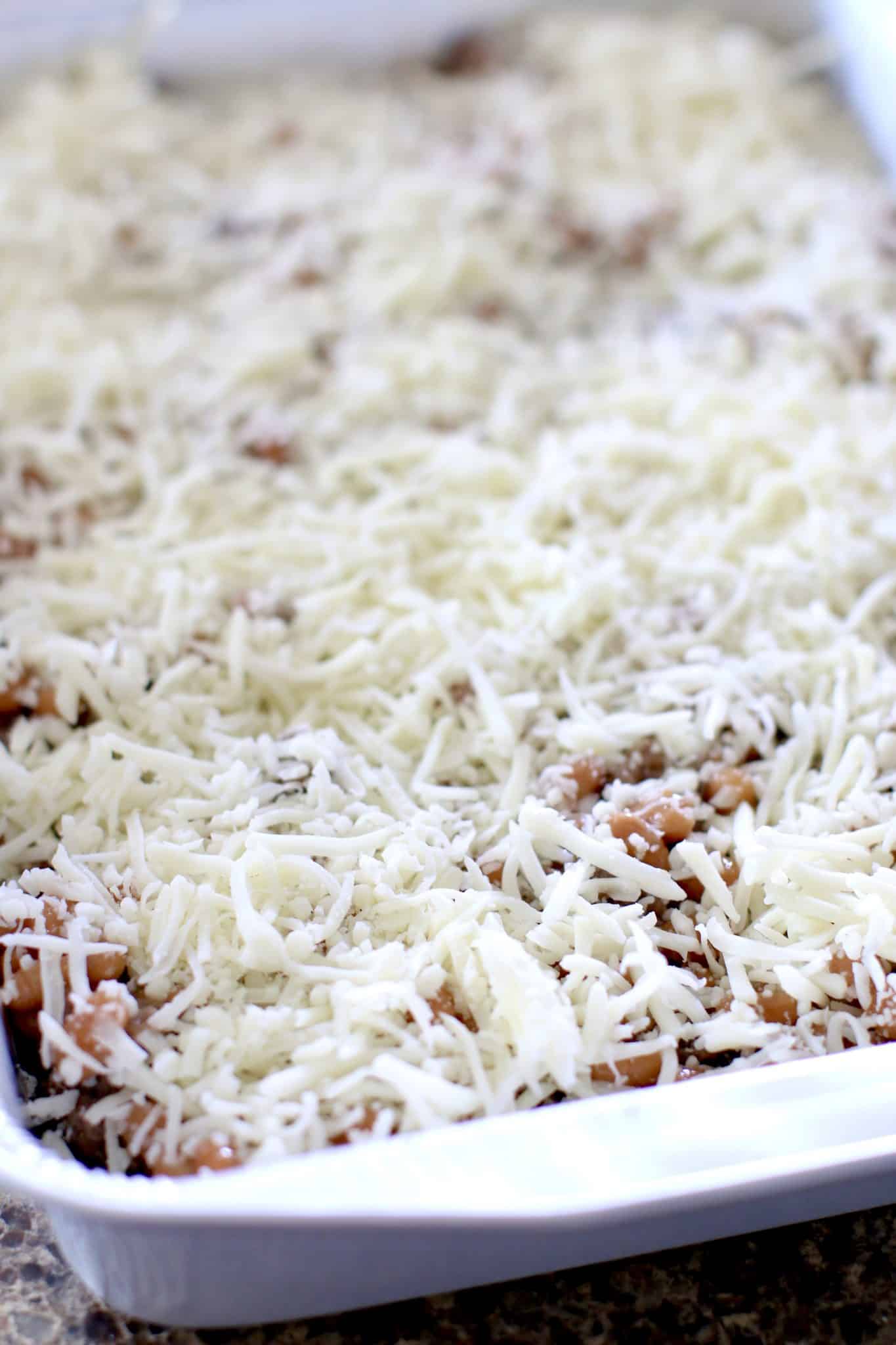shredded cheese layered on beans in baking dish. 