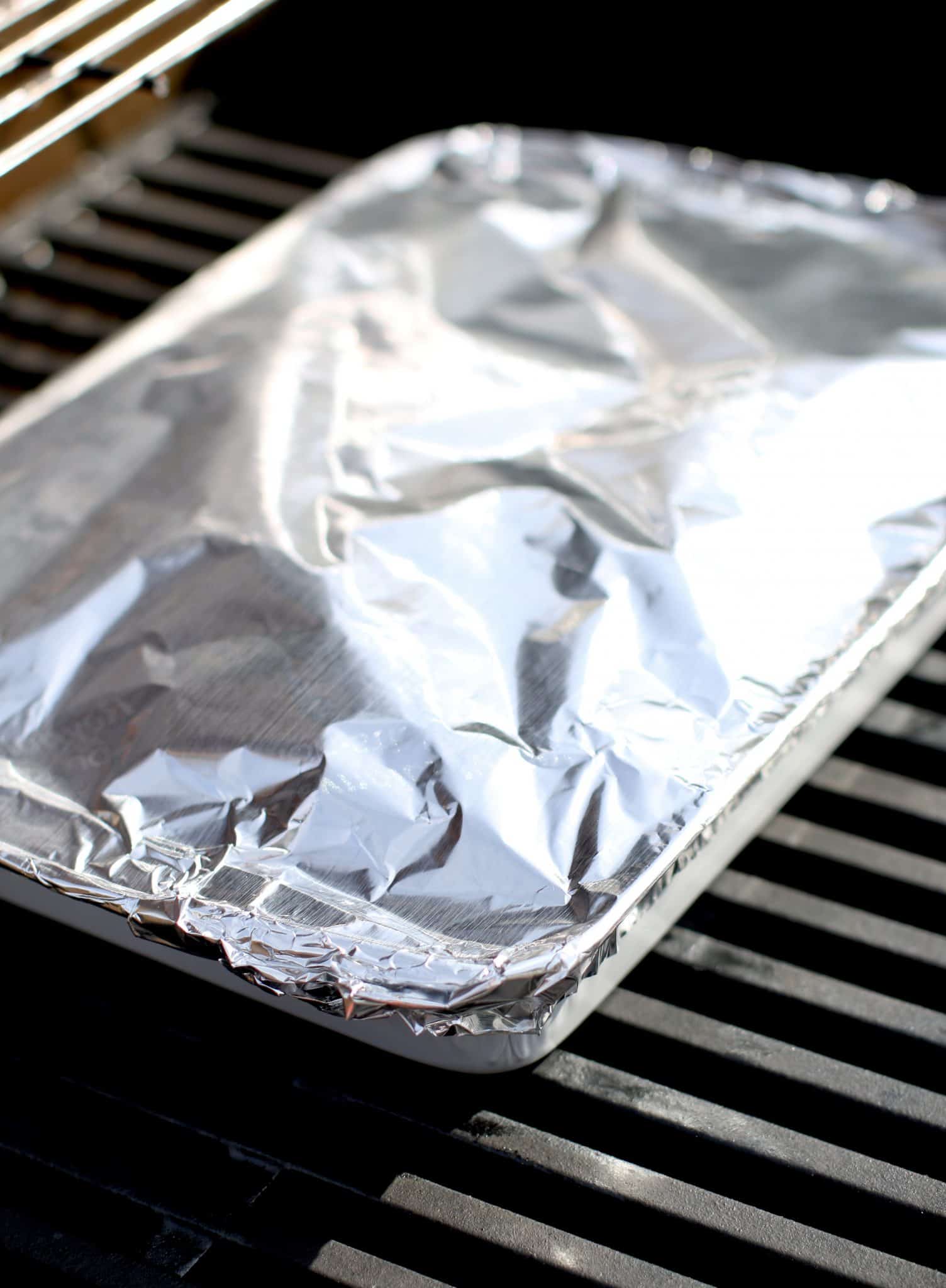 aluminum foil covered baking dish shown on an outdoor grill. 
