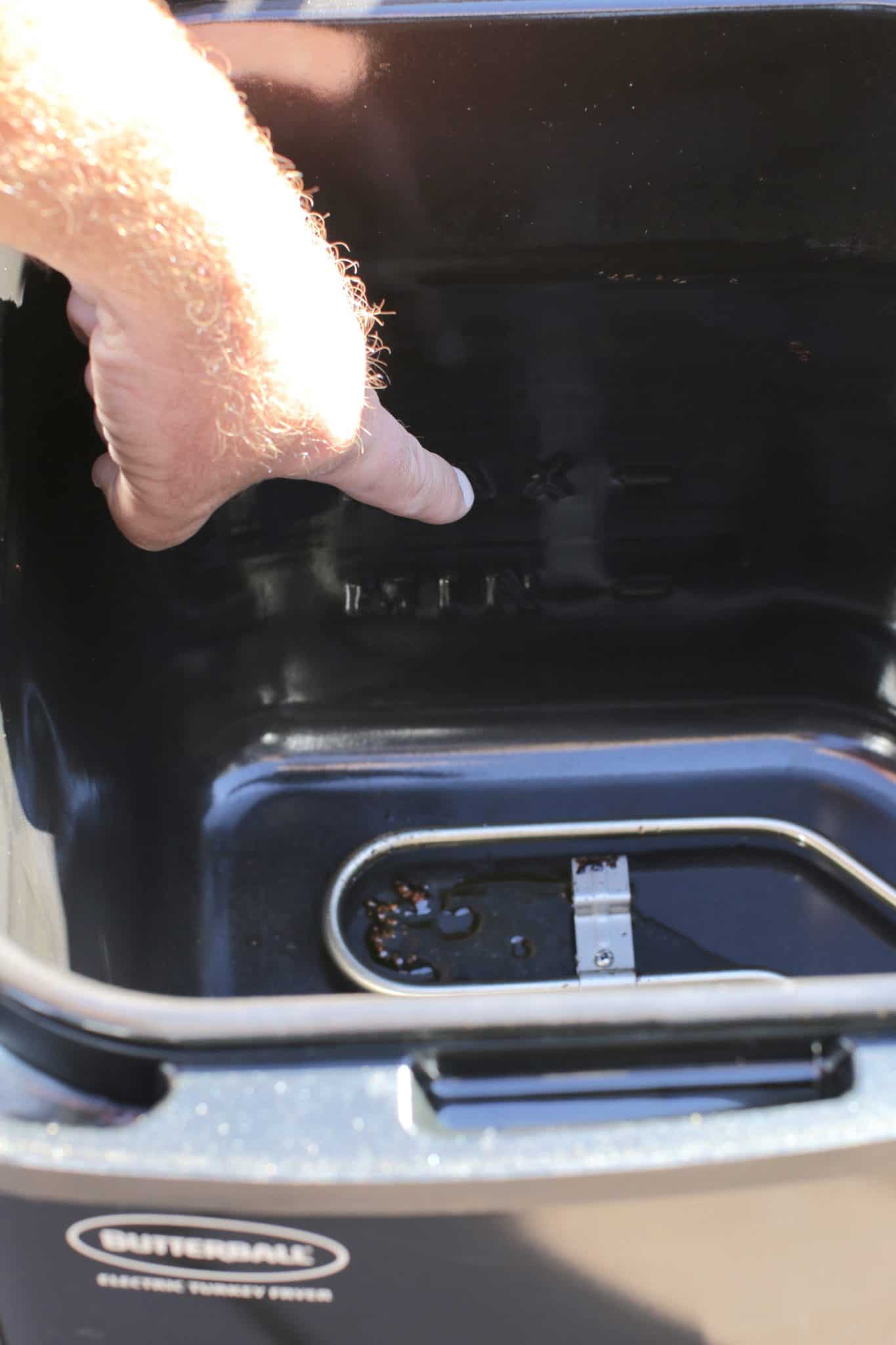a male finger pointing at a fill line inside a turkey fryer. 