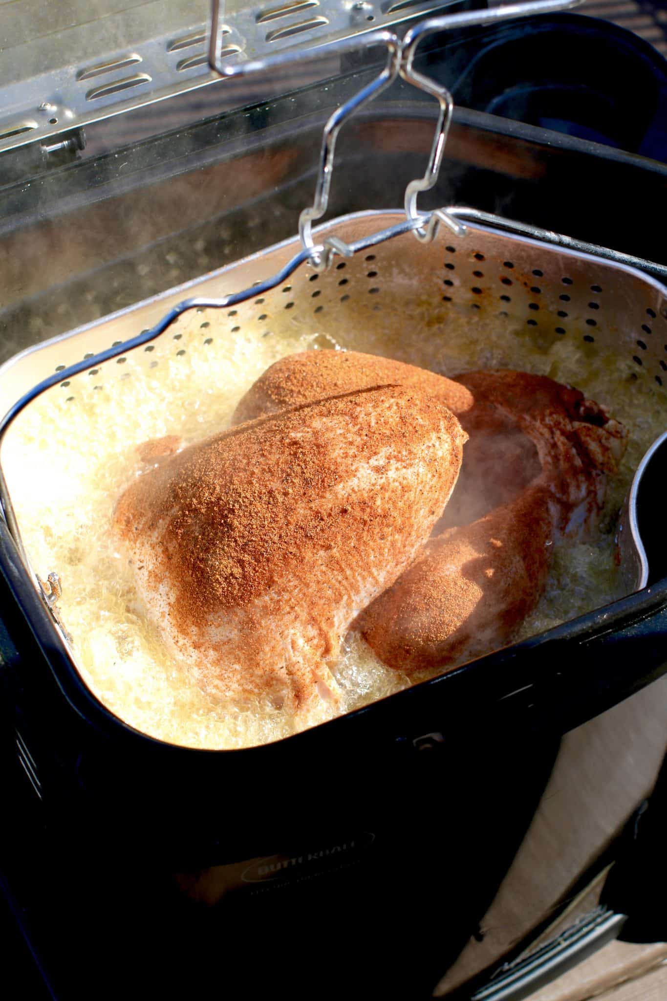 whole turkey inside a fryer basket being lowered into the oil of an electric turkey fryer. 