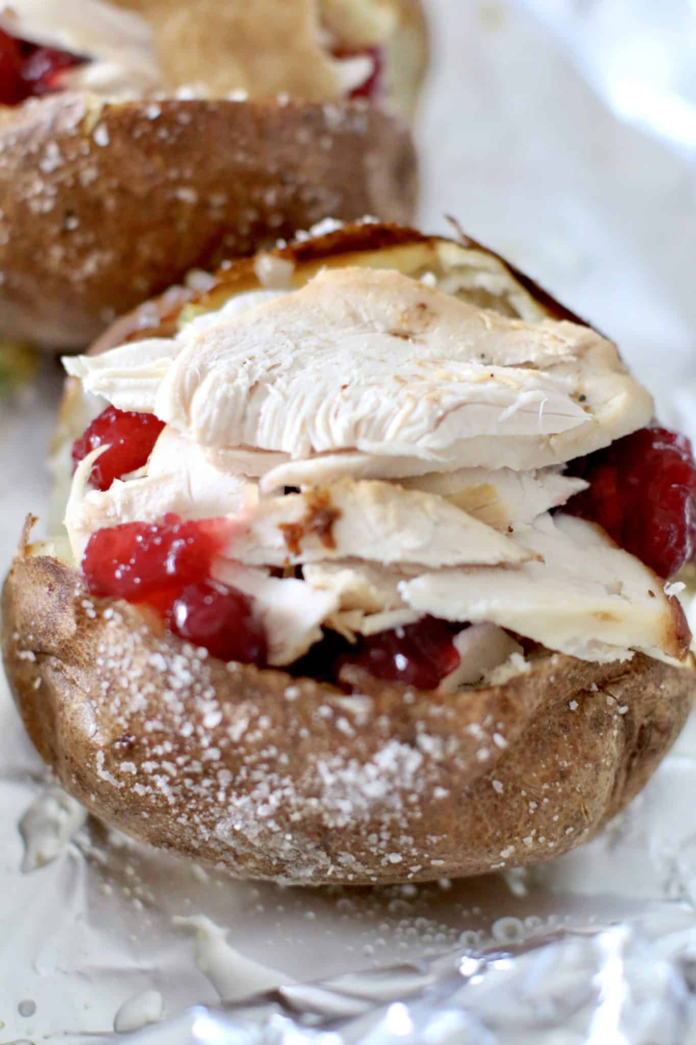 sliced turkey layered on top of cranberry sauce in sliced baked potato.