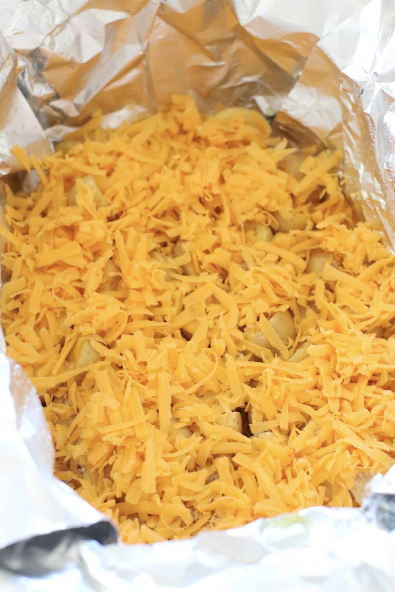 shredded cheese shown layered on top of diced potatoes in an oval slow cooker. 
