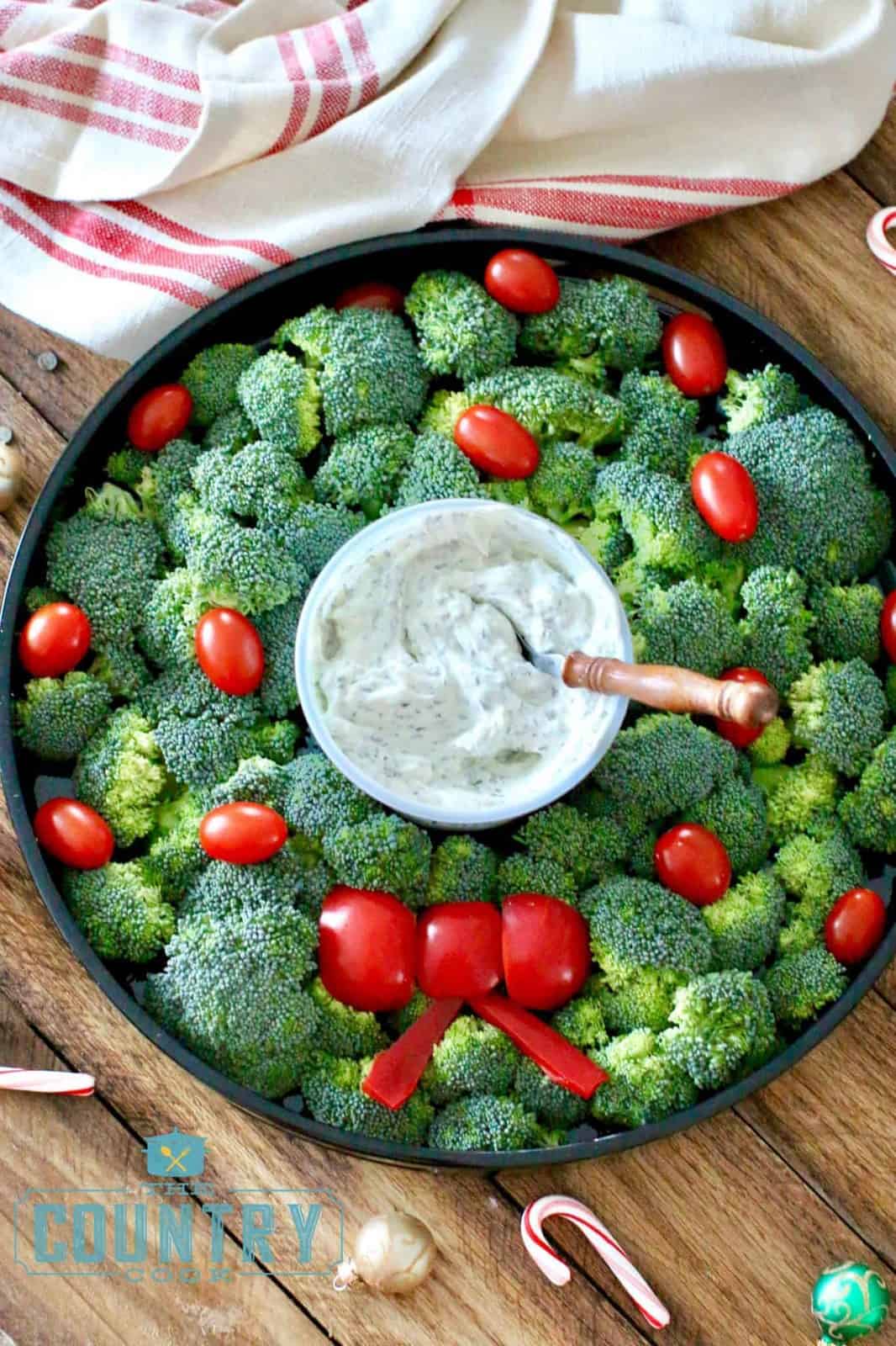 a close up photo of the vegetable Christmas wreath made in a circle using broccoli florets, grape tomatoes and red peppers.