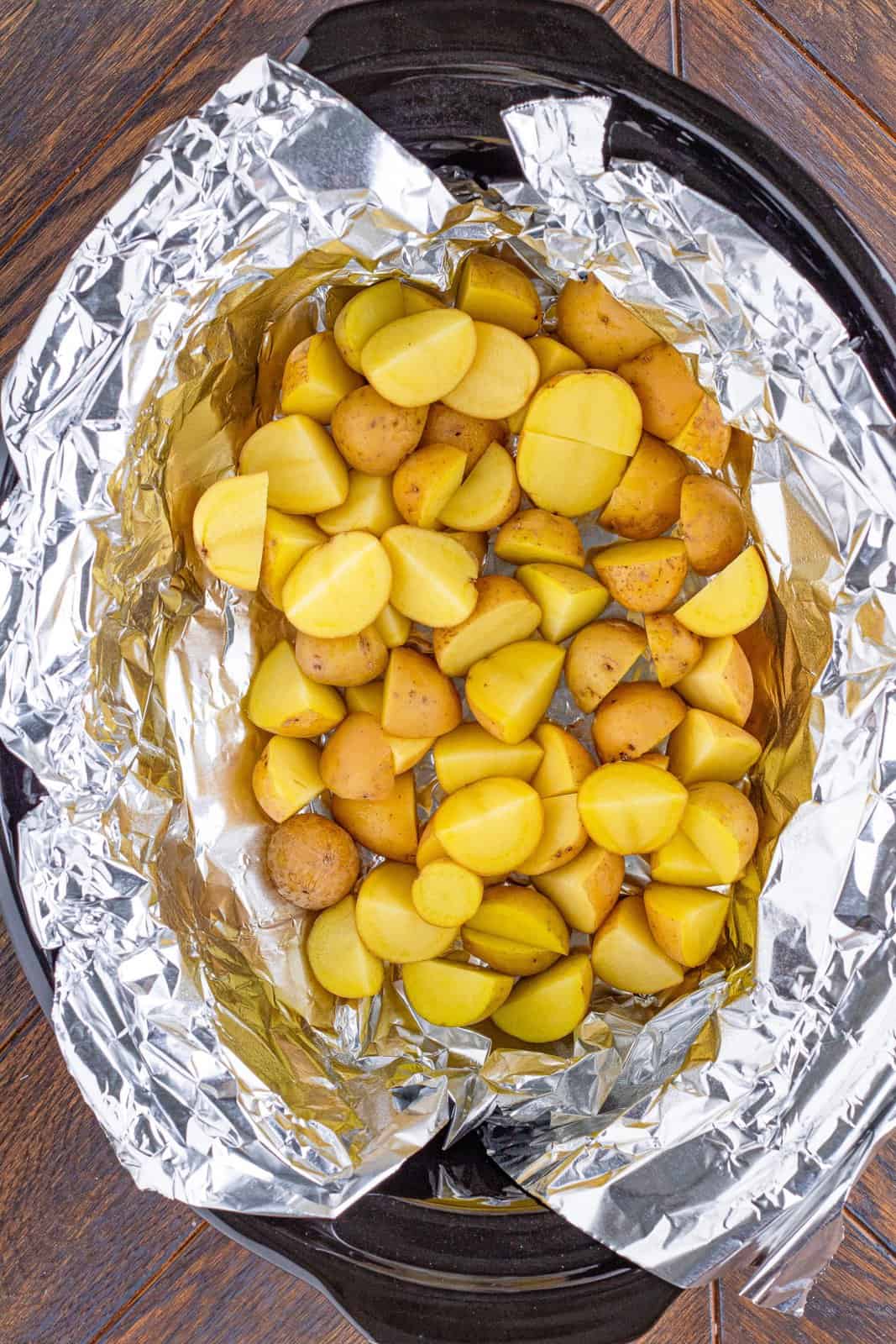sliced potatoes evenly placed into the bottom of a slow cooker. 