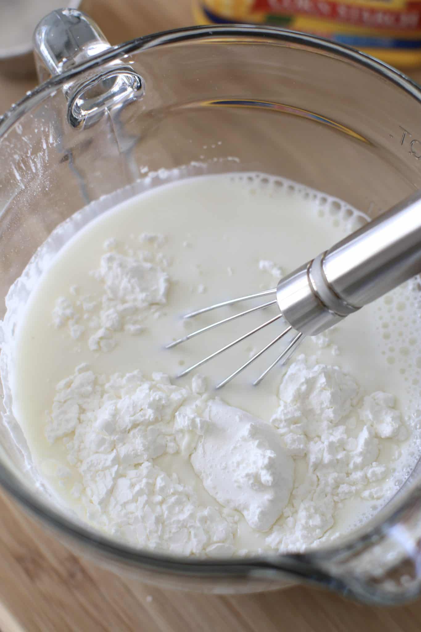 cornstarch and milk mixed together with a small whisk in a clear measuring cup.