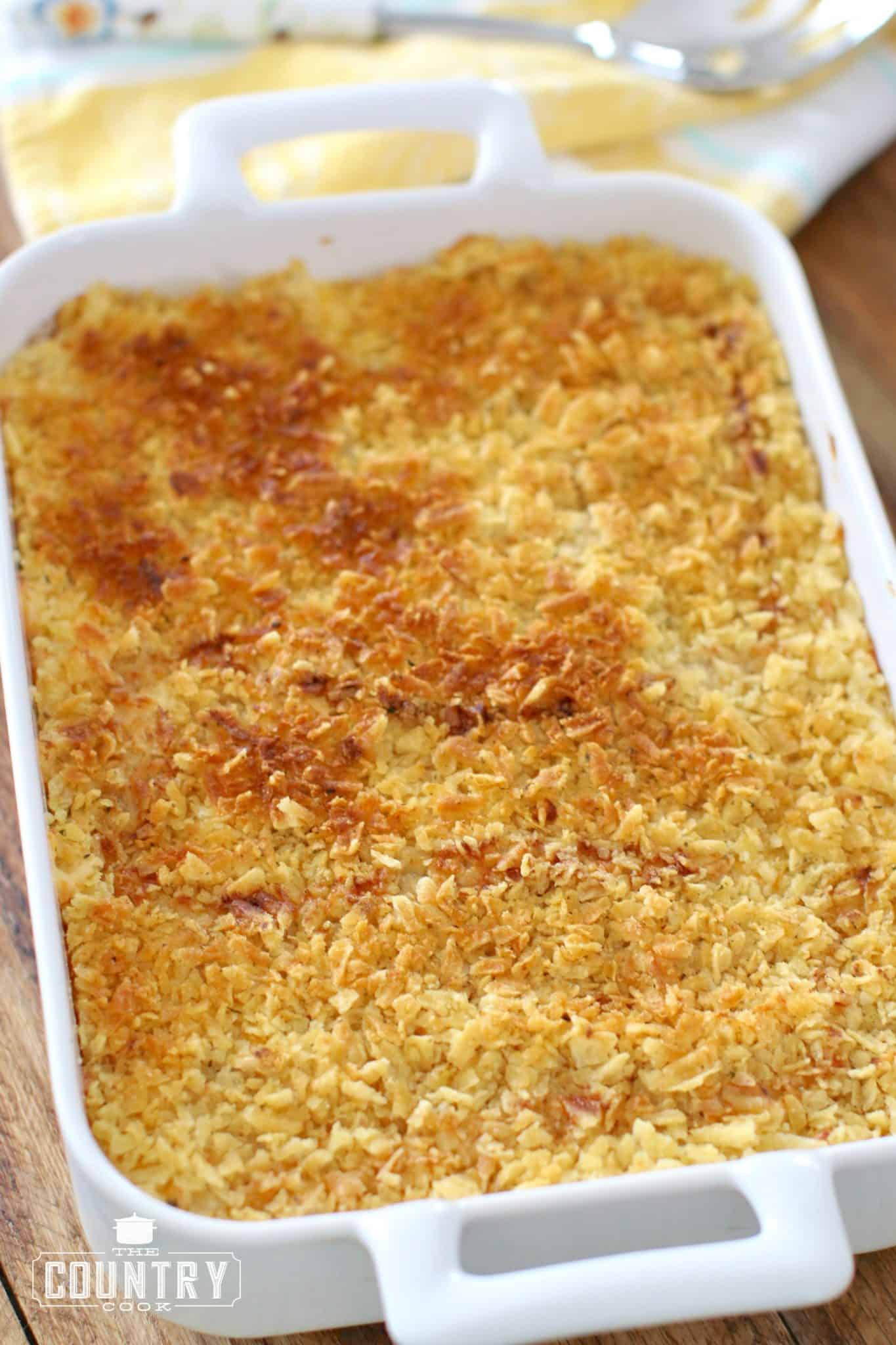 Funeral Potatoes, finished, shown in a white casserole dish, crushed potato chips shown browned.