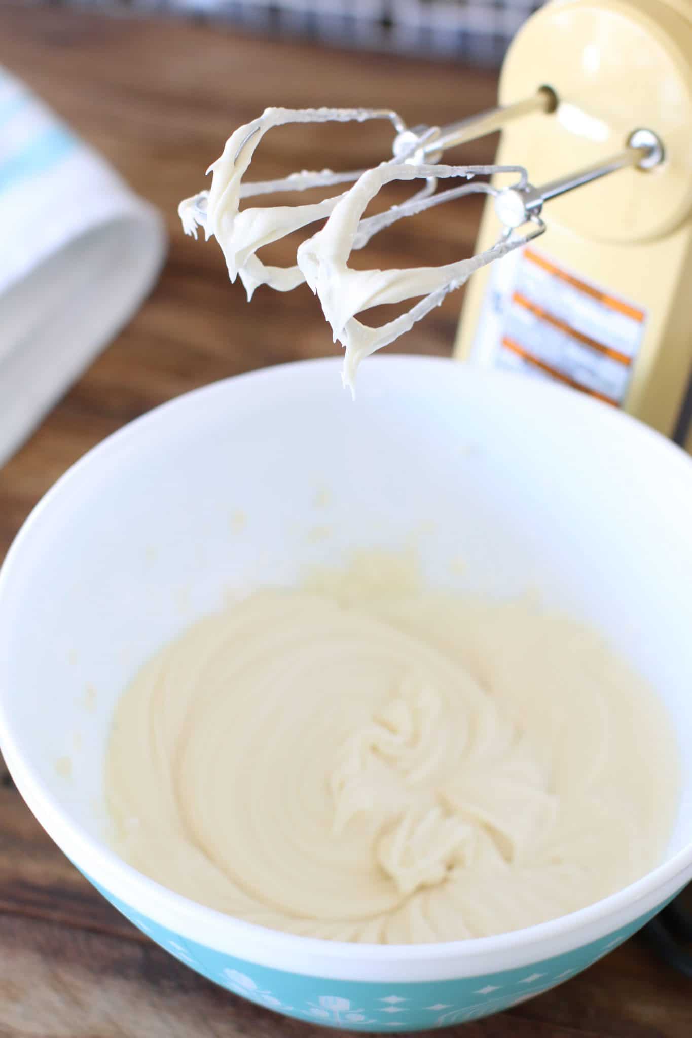 whipped frosting in a bowl with an electric hand mixer propped up in the background. 