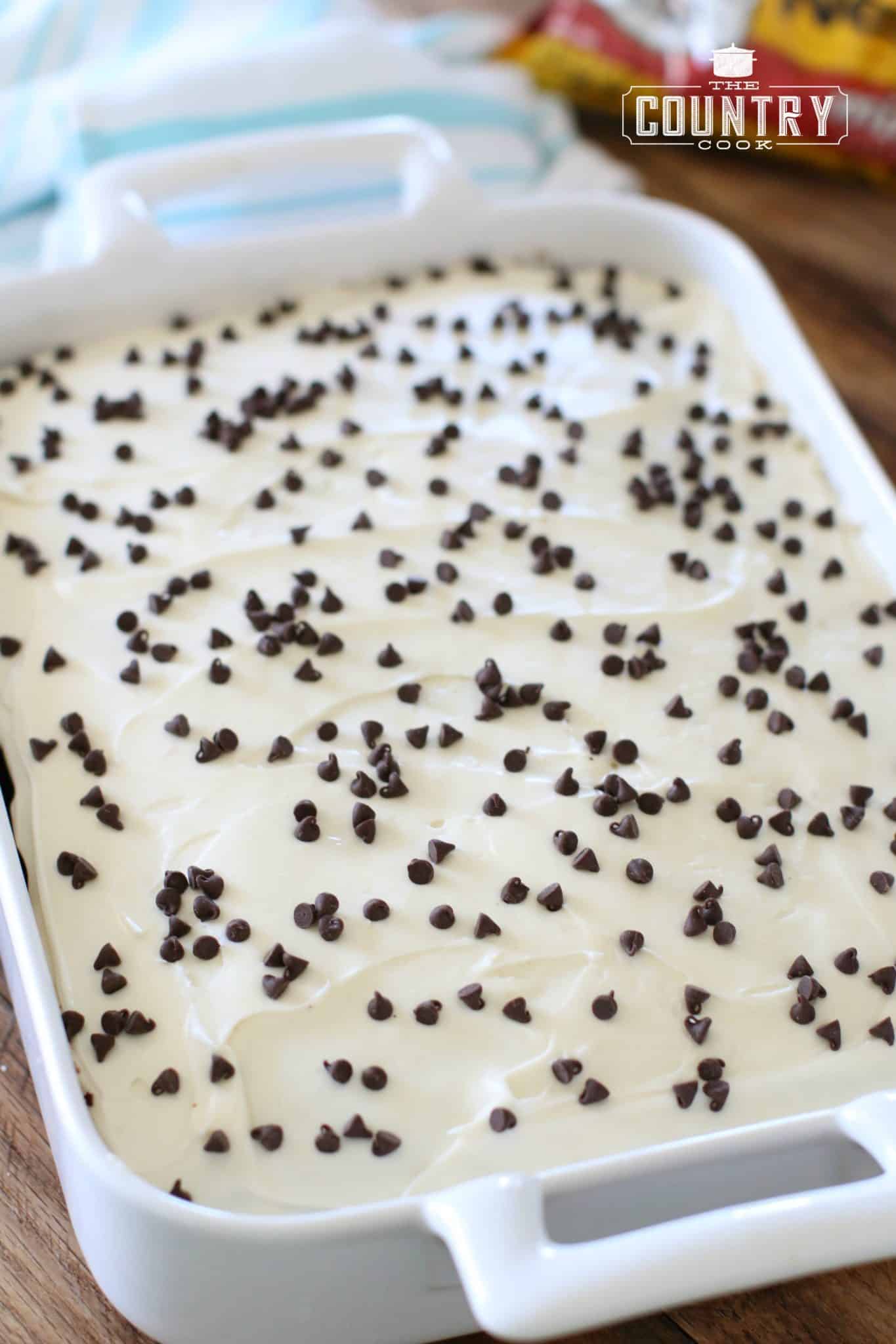 fully baked chocolate cake in a rectangular baking dish and topped with vanilla frosting and mini chocolate chips.