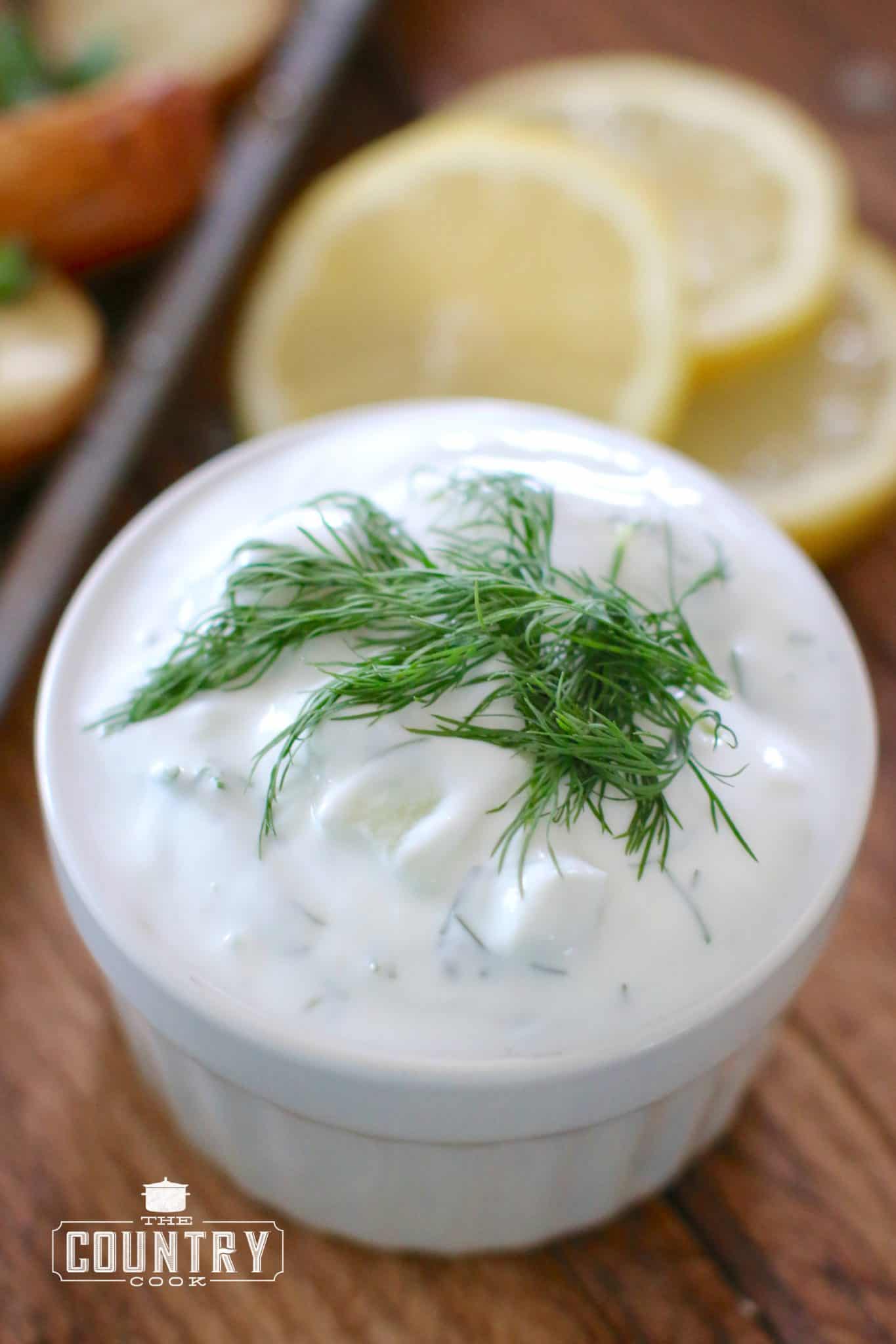 Tzaziki Sauce shown in a small white serving bowl with fresh dill laid on top.
