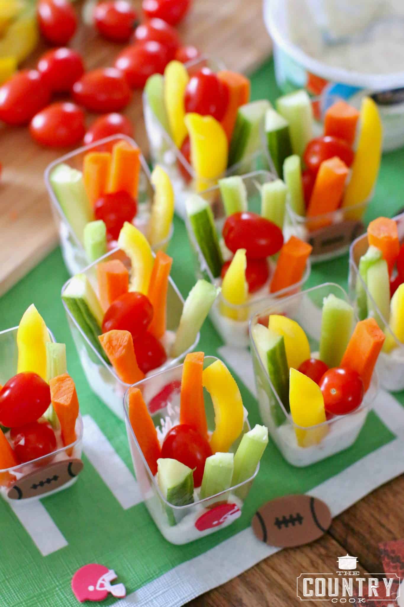 individual veggie dip cups on a football patterned table cloth.