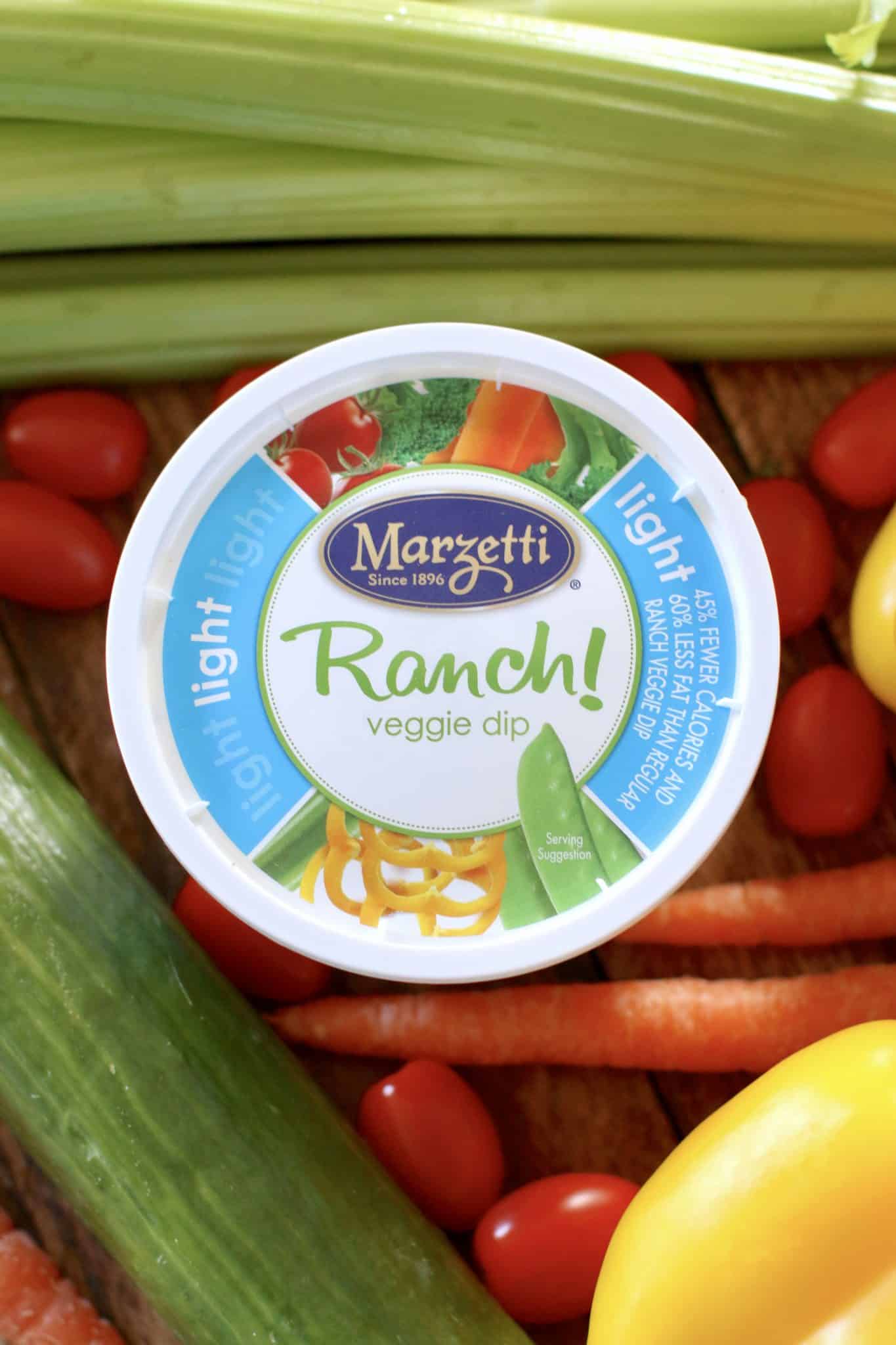 a tub of ranch dressing surrounded by fresh vegetables.