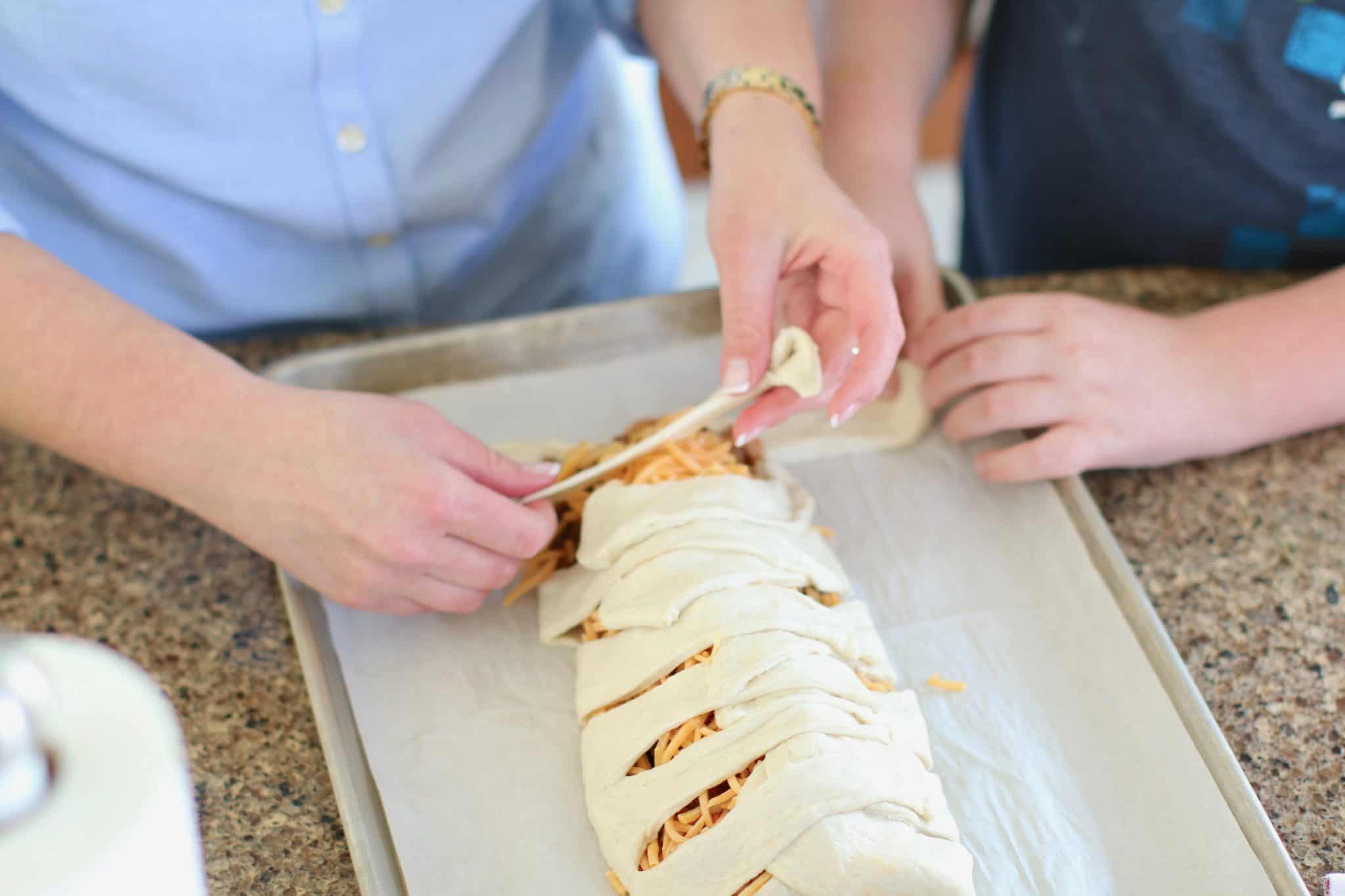 two sets of hands braiding pizza dough over taco filling. 
