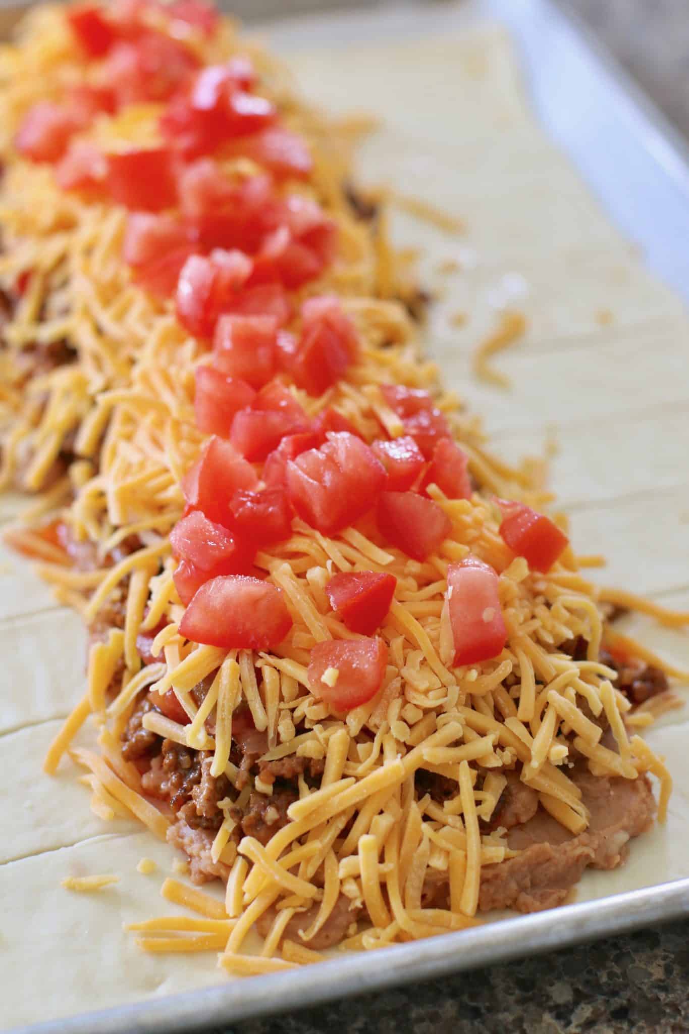 diced tomatoes shredded cheese layered on top of ground beef and refried beans. 