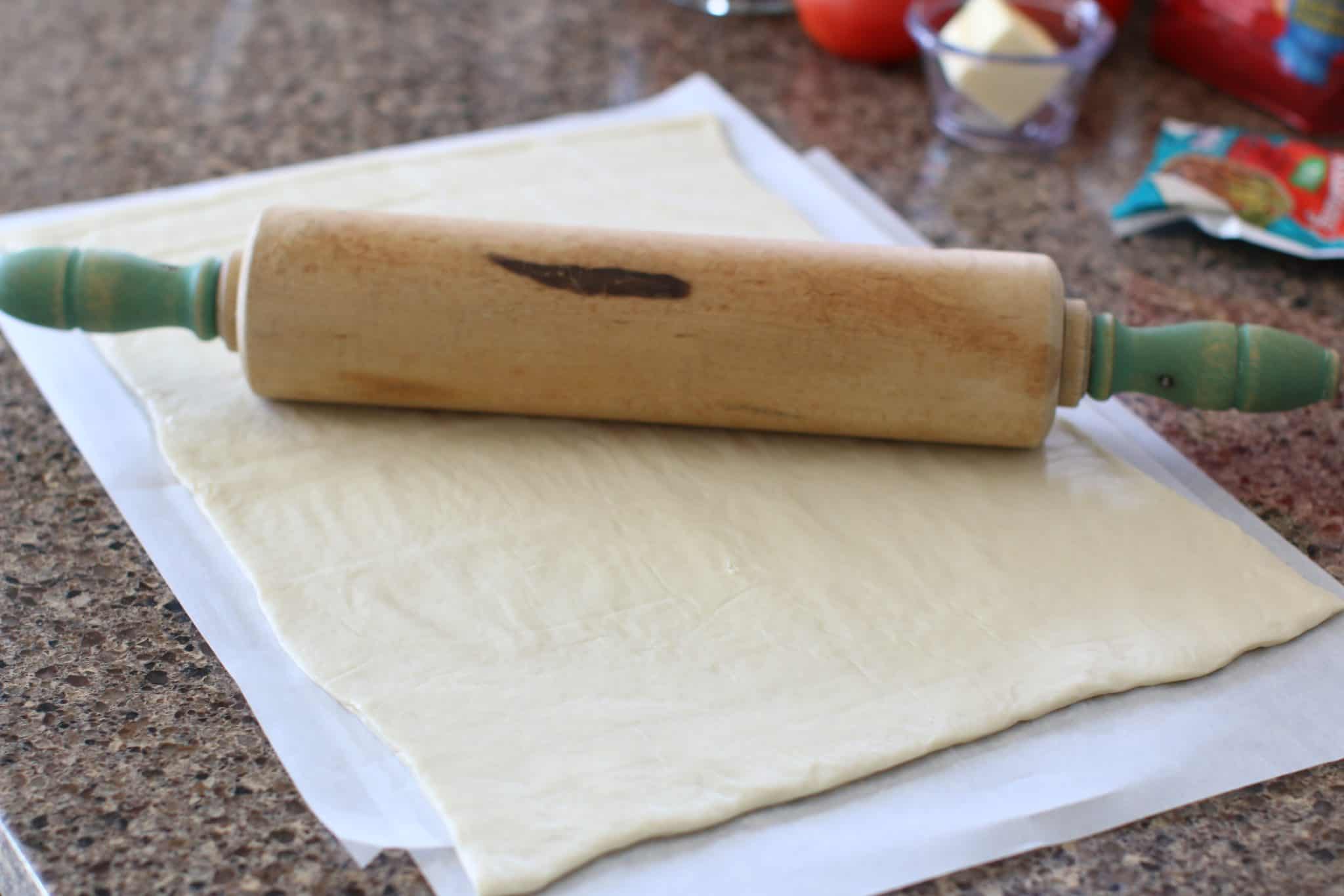 a wooden rolling pin rolling out pizza dough. 