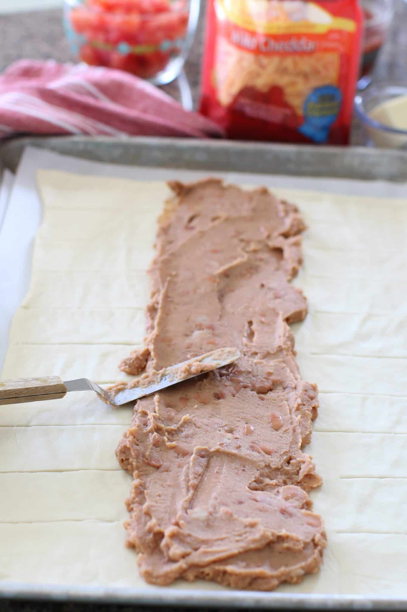 an offset spatula spreading refried beans onto pizza crust. 