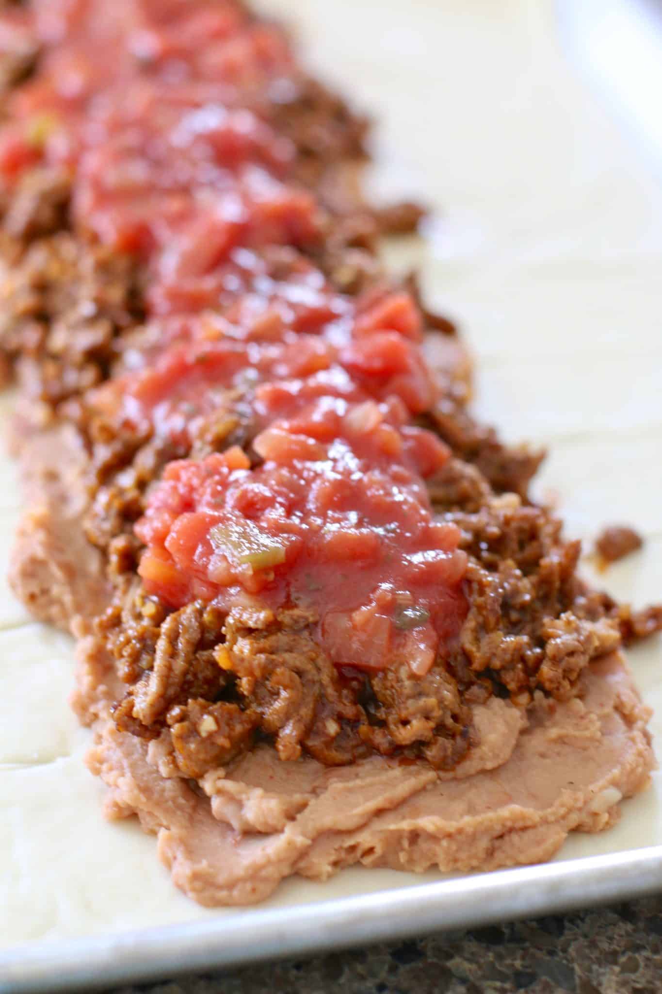 salsa spread on top of ground beef and refried beans. 
