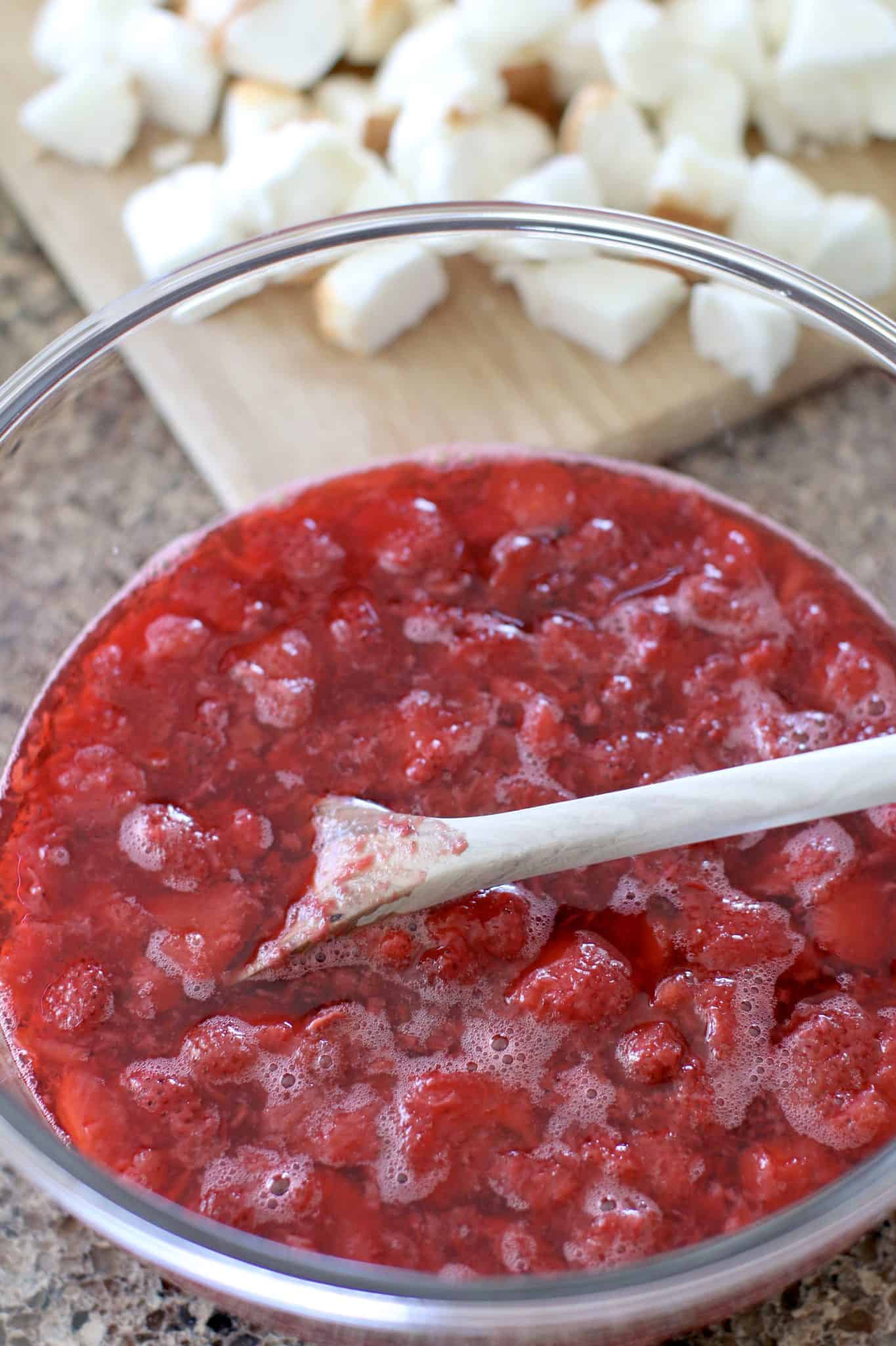 frozen strawberries mixed together with strawberry gelatin mixture in glass mixing bowl.