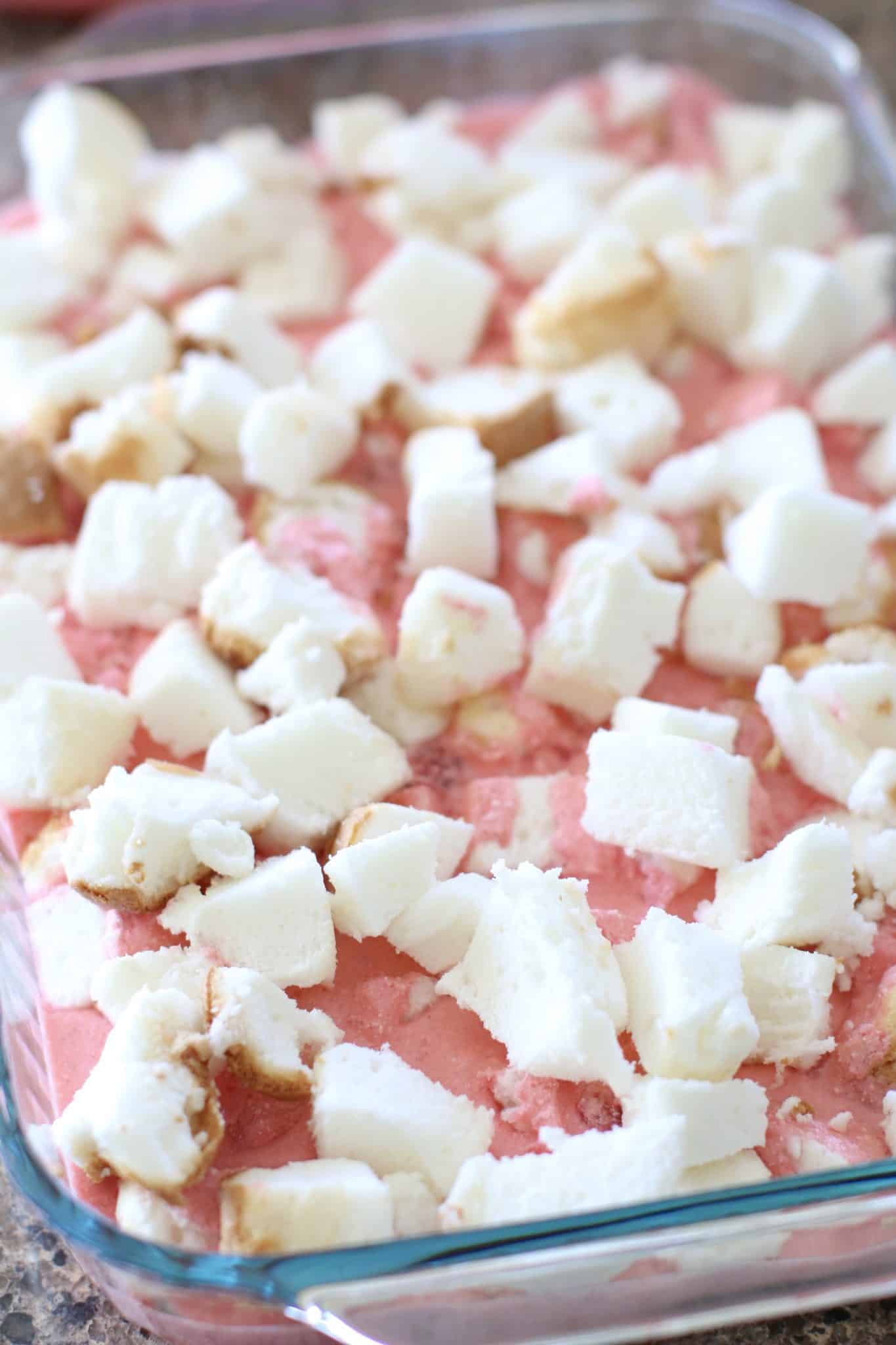 a layer of diced angel food cake spread out evenly on top strawberry gelatin mixture in baking dish.