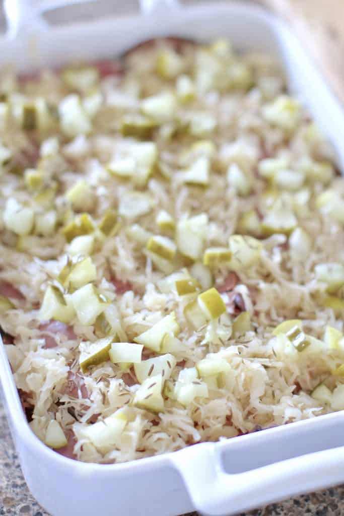 chopped pickles and sauerkraut layered on sliced pastrami in a casserole dish.