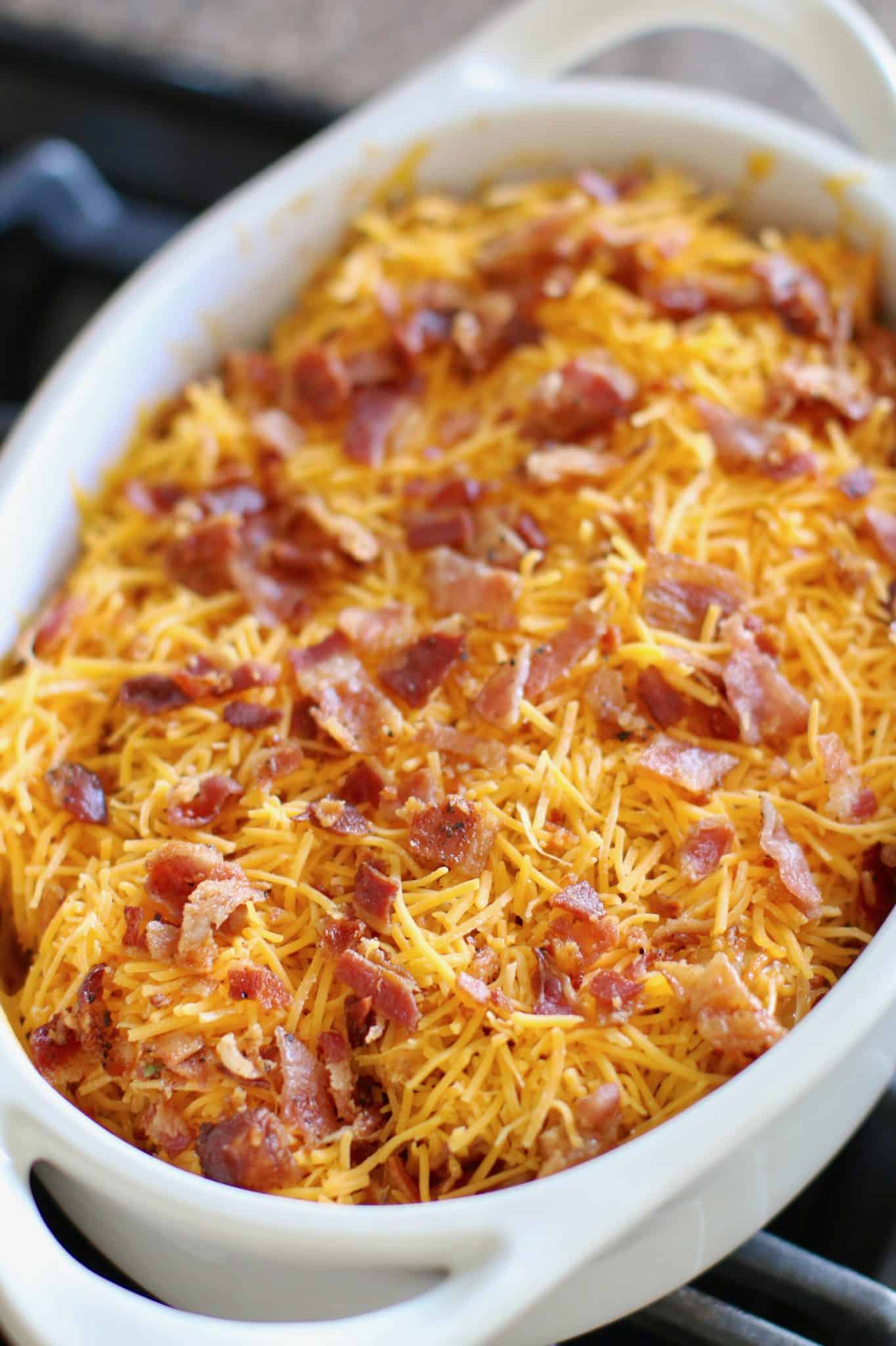 shredded cheese and chopped bacon shown covering the tex Mex potatoes in the white oval baking dish. 
