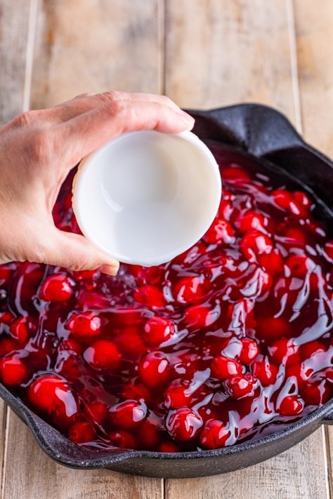 Almond extract being dumped in a skillet with cherry pie filling.